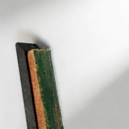 Close-up of the strop edge: tan leather with green compound rubbed in, on the thin black base